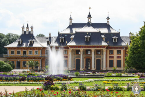 Das bunte Schloss Pillnitz mit Springbrunnen und bluehendem Garten davor