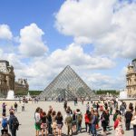 Menschen im Vordergrund die Glaspyramide des Louvre Museums im Hintergrund Zu Besuch in Paris