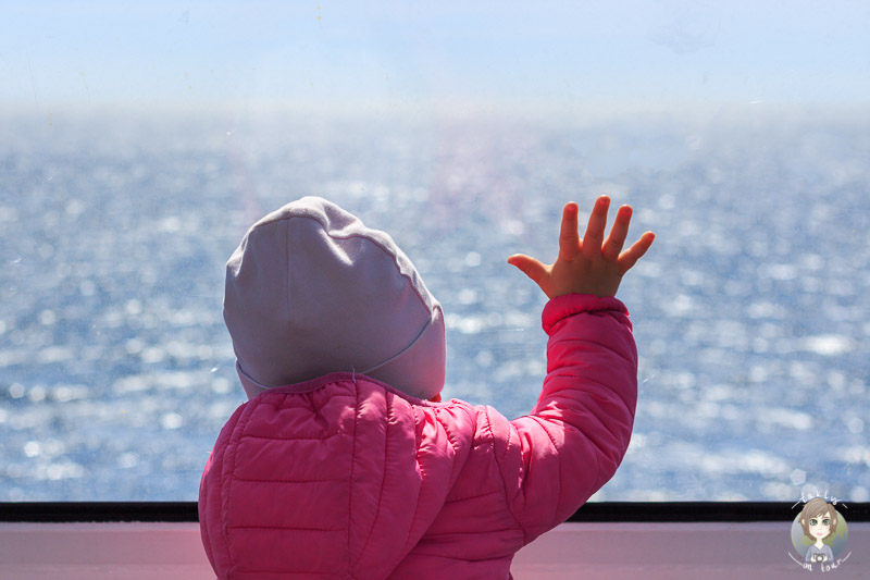 Ein Kleinkind schaut während einer Fernreise mit Baby durch eine Scheibe auf das Meer